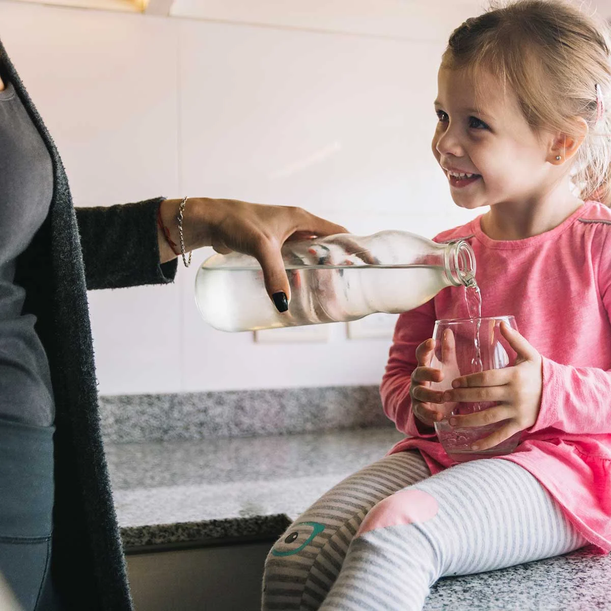 woman-s-hand-pouring-water-glass-her-happy-daughter